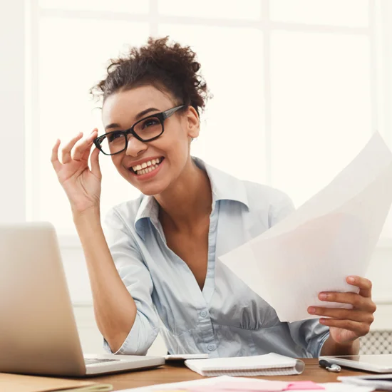 Woman smiling adjusting glasses while working on laptop