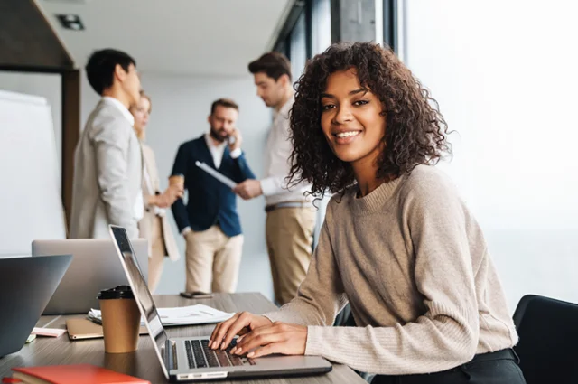 businesswoman working on laptop facing outward smiling