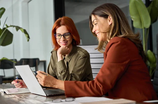 female colleagues smiling looking at laptop reviewing employee benefits info